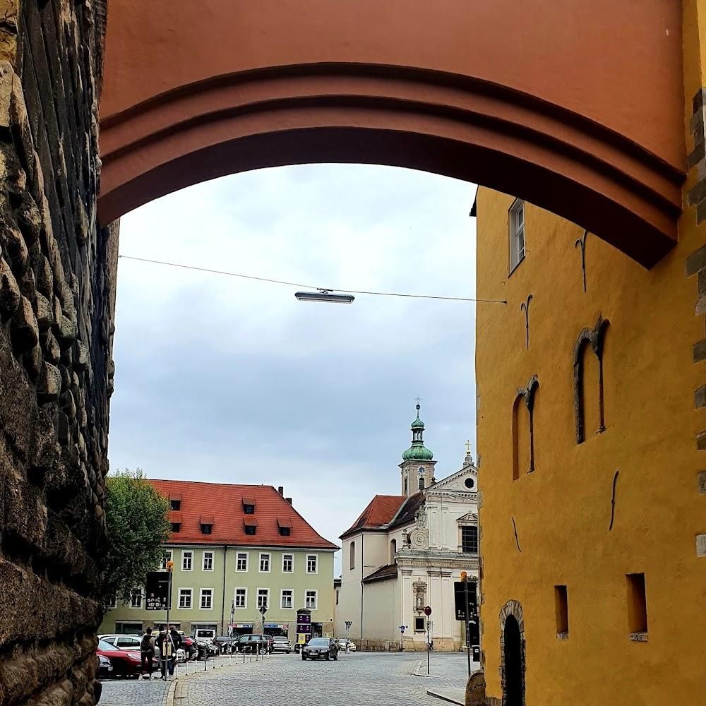 Stone archway, yellow building, church, street, cars. Landmark: The Church of the Assumption of the Virgin Mary.